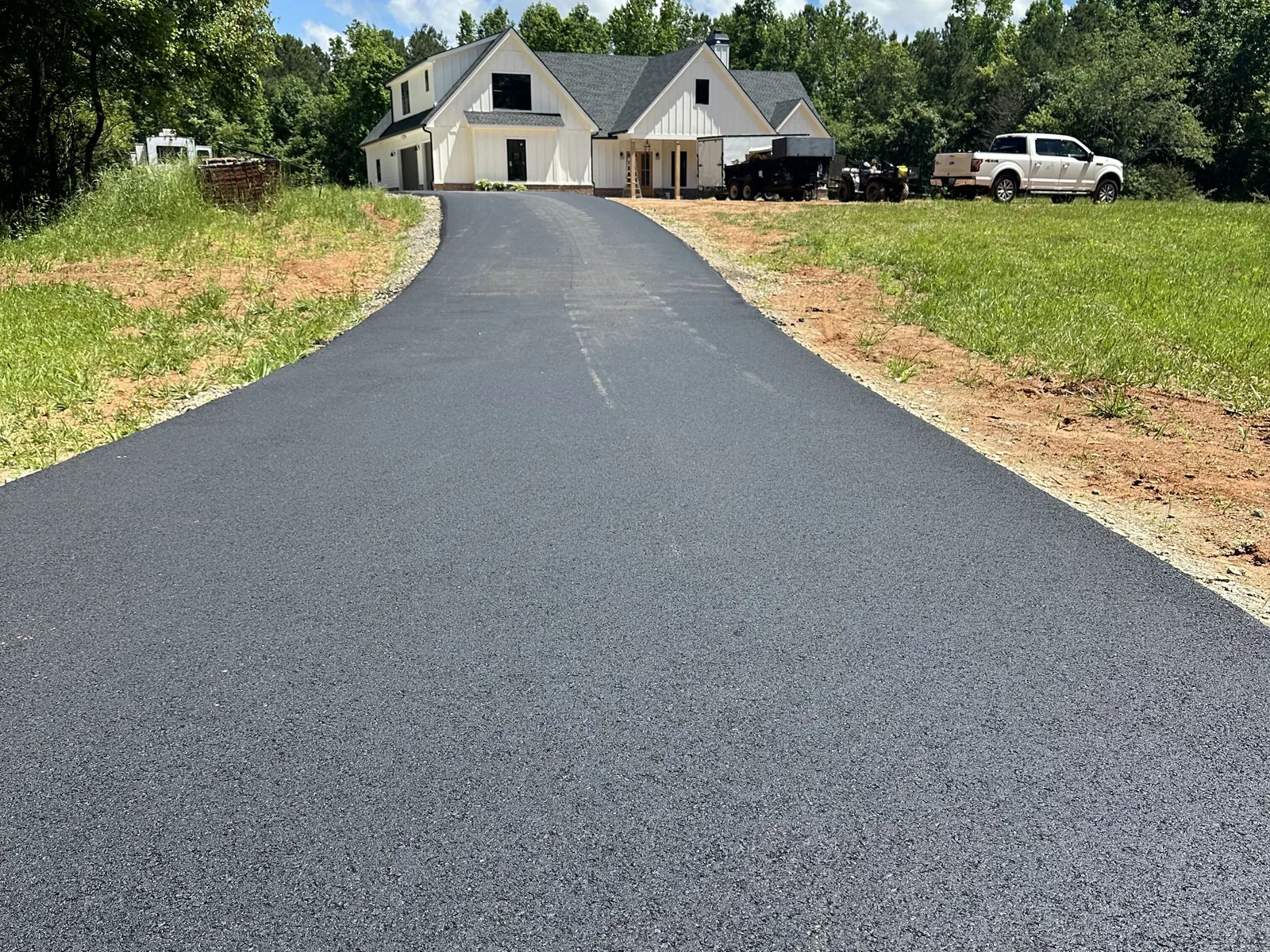 Long new asphalt driveway running up to a white farmhouse with the company truck and trailer parked beside it