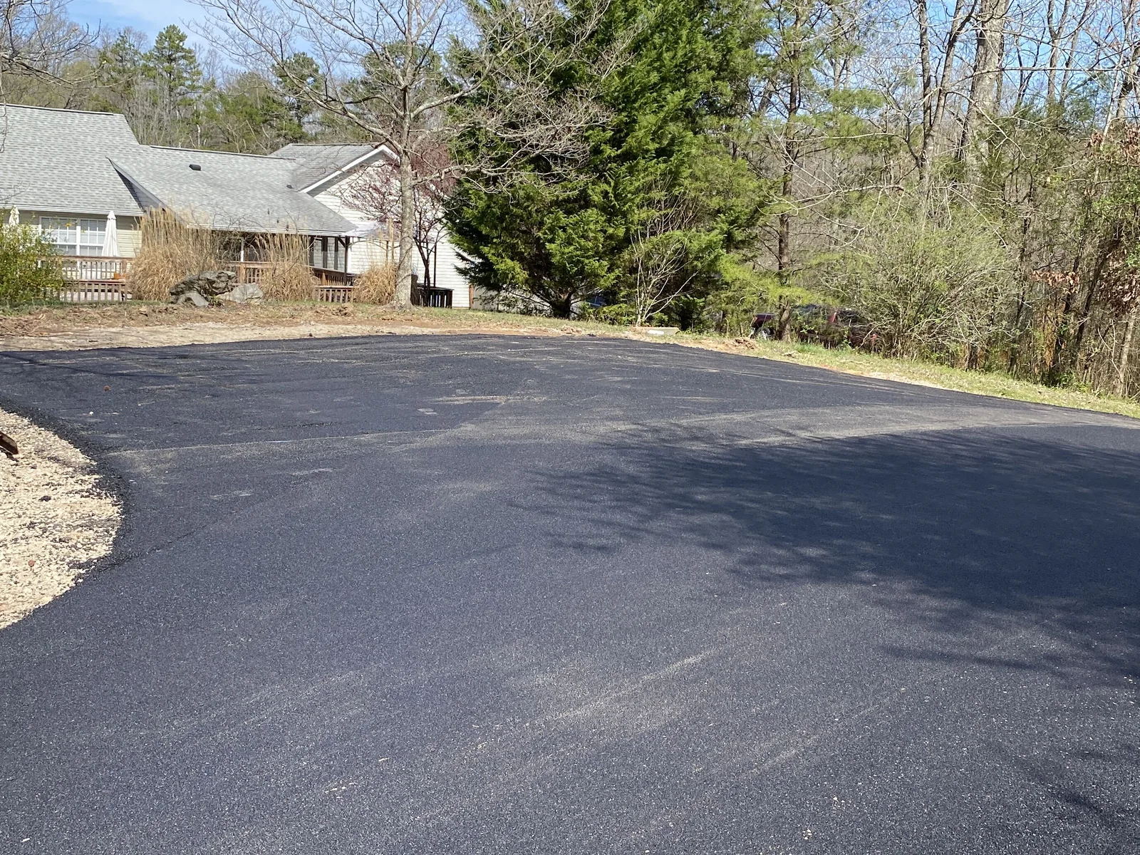 Fresh asphalt driveway looping in front of a ranch home with a deck and a tall evergreen