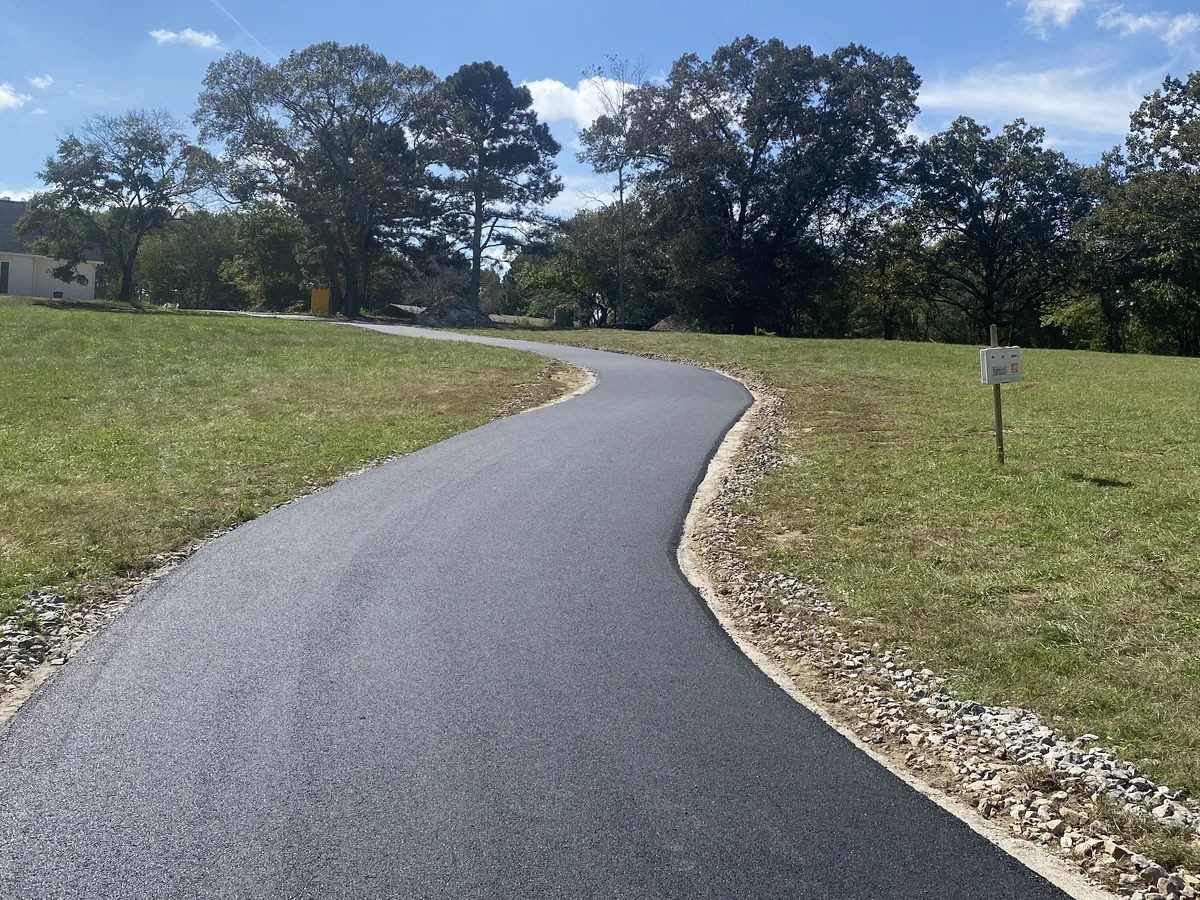 Fresh asphalt driveway with a clean stone shoulder curving across a pasture
