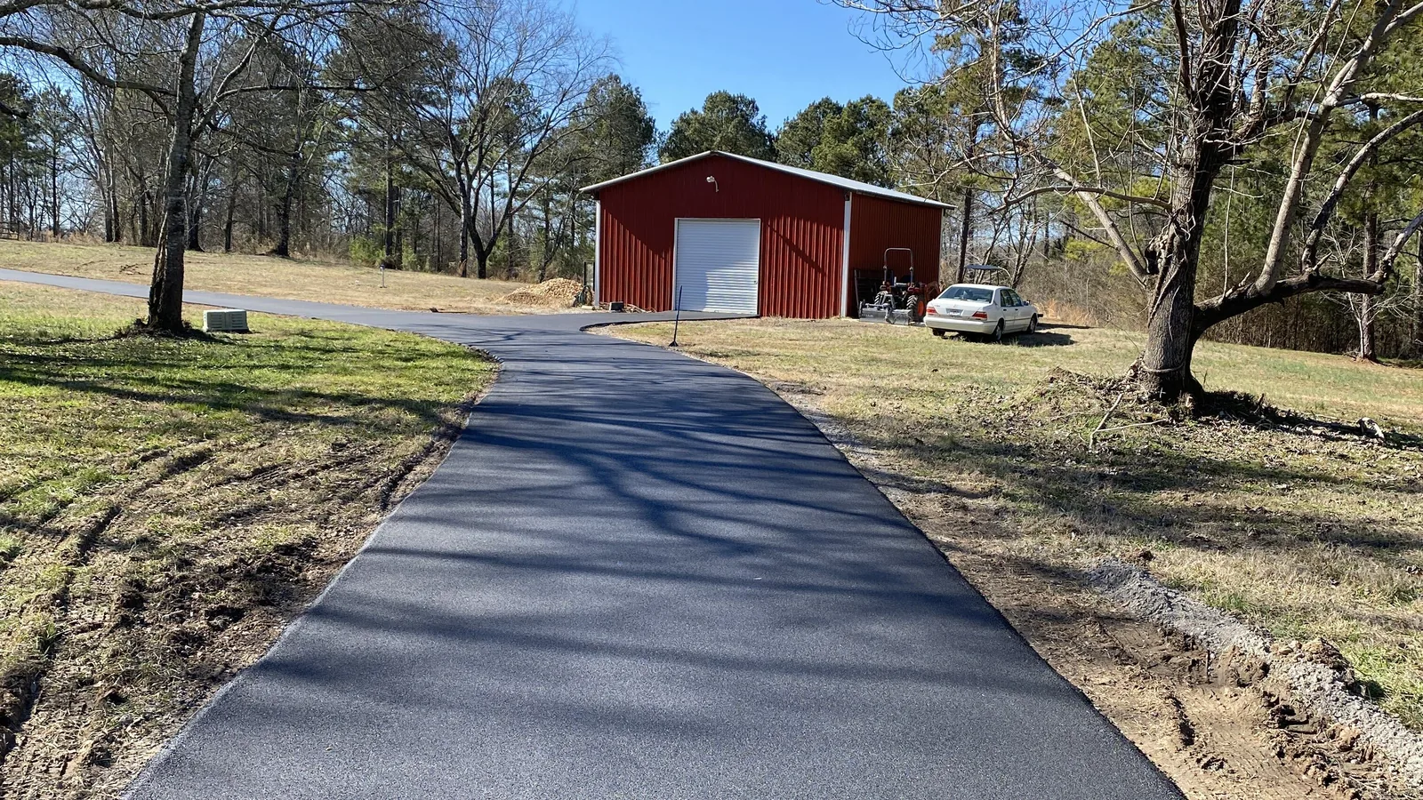 New asphalt driveway running up to a red metal barn on a rural lot