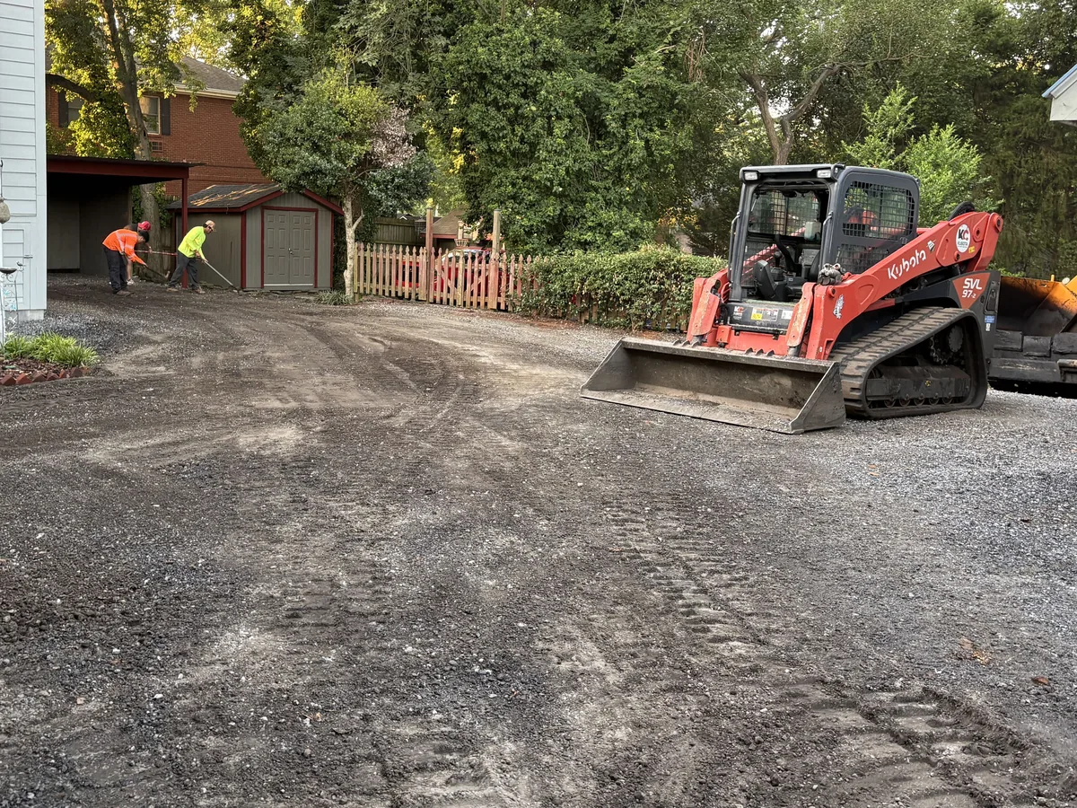 Track loader spreading and grading the crushed stone base before paving, with crew in hi-vis