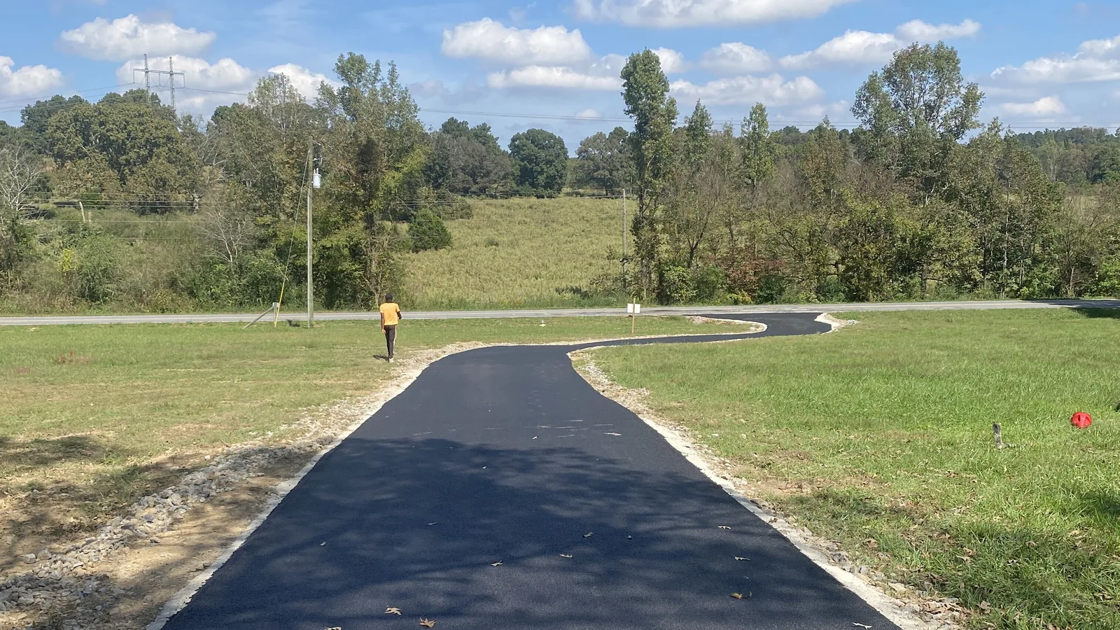 Long new asphalt drive running straight across an open field under a big cloudy sky