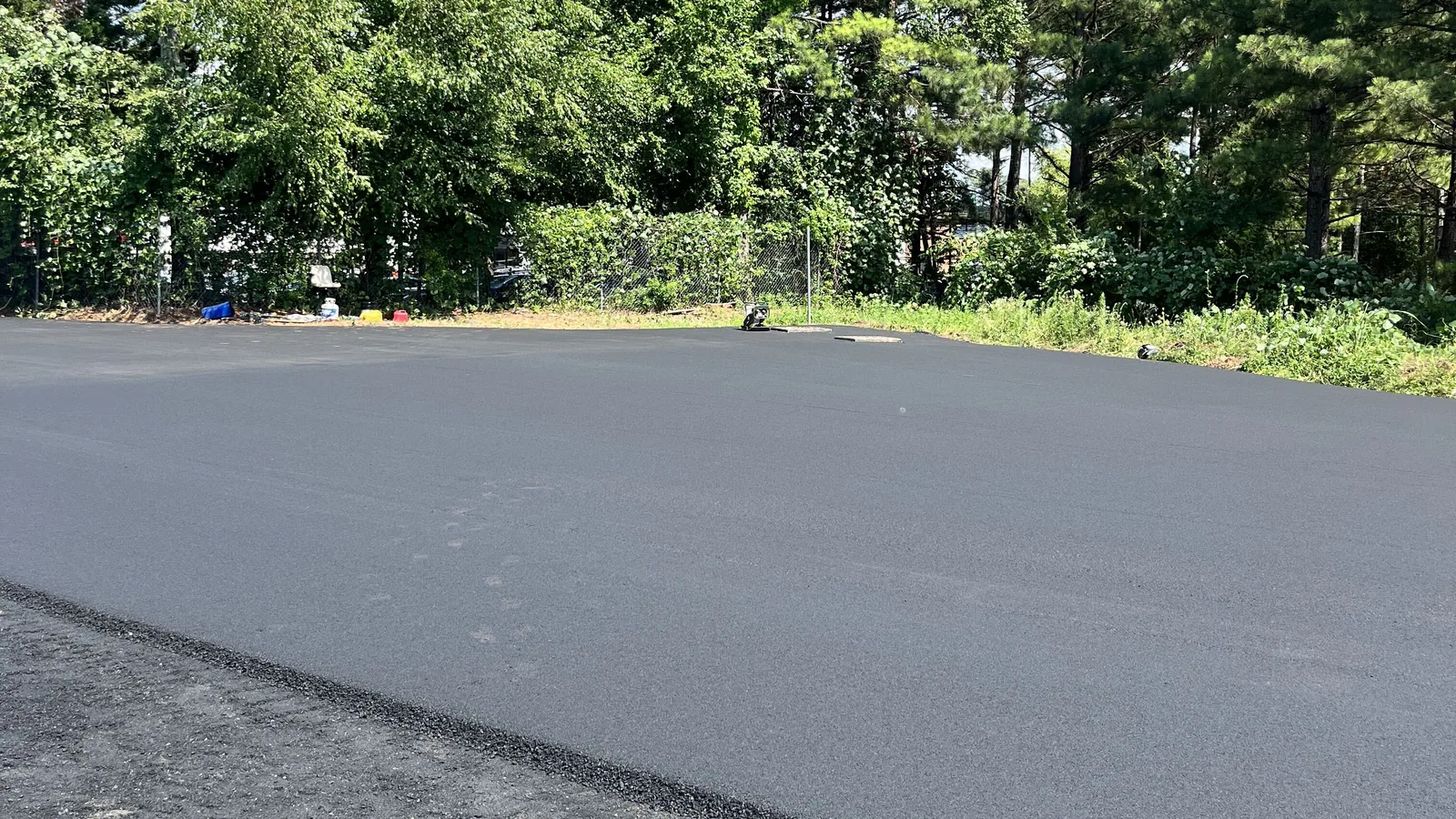 Large freshly paved asphalt lot stretching back toward the tree line