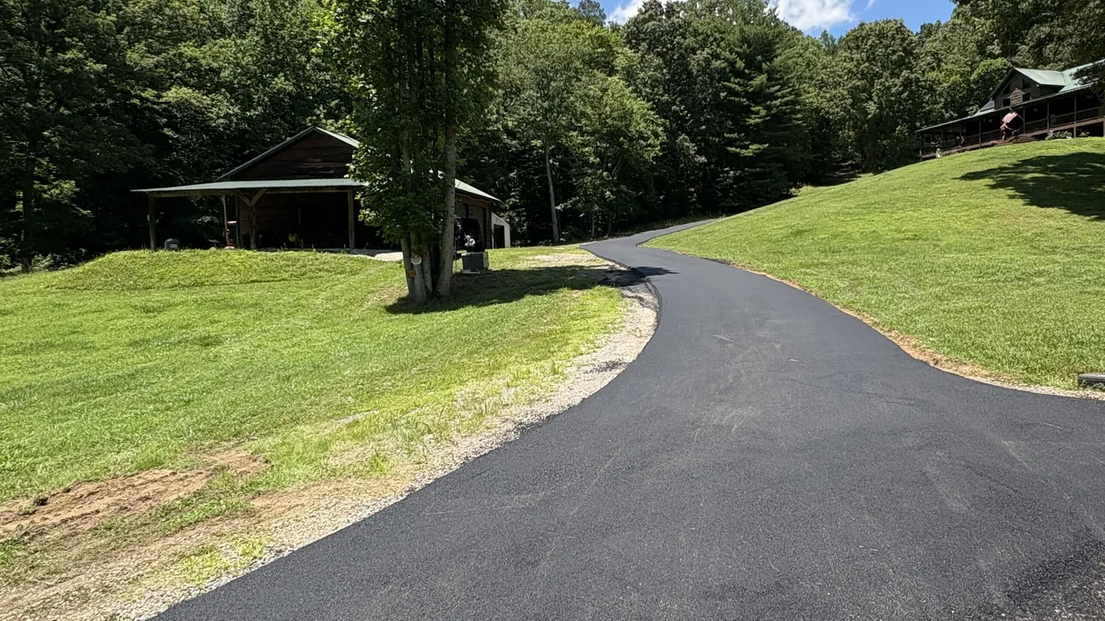 Fresh asphalt driveway curving uphill across a green lawn toward a home