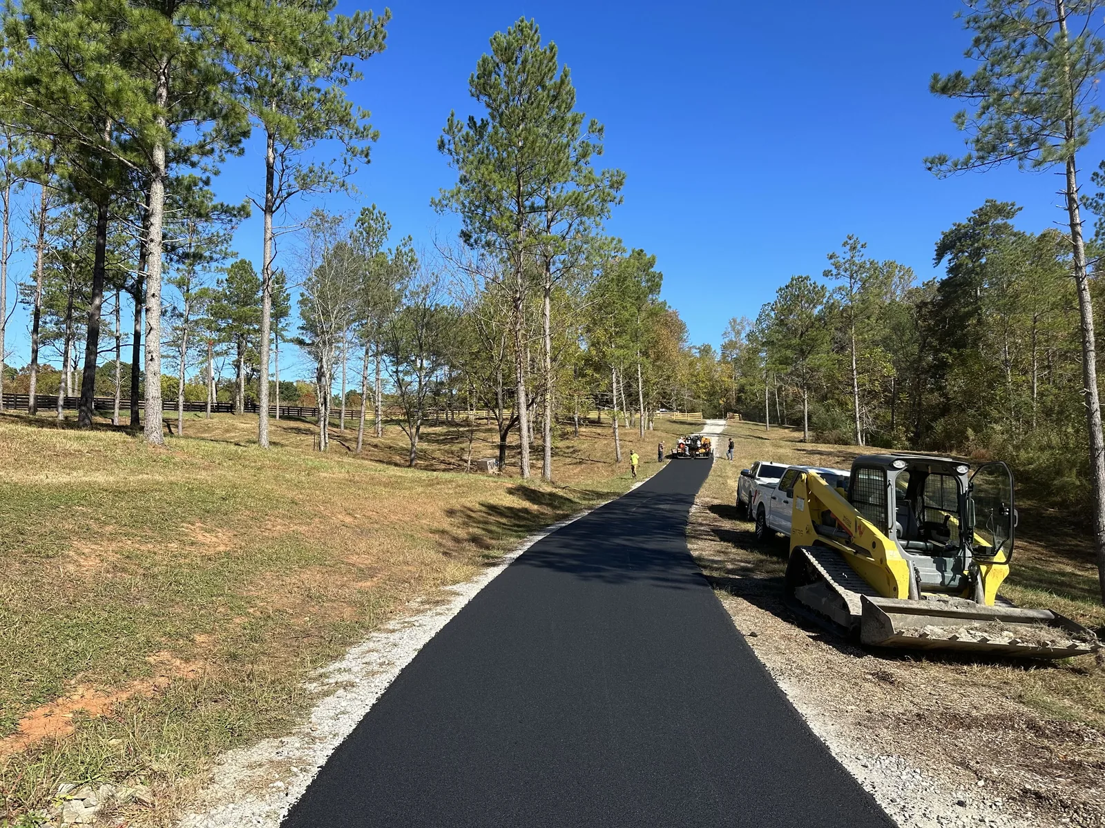 New asphalt lane through a pine stand with a track loader parked on the shoulder