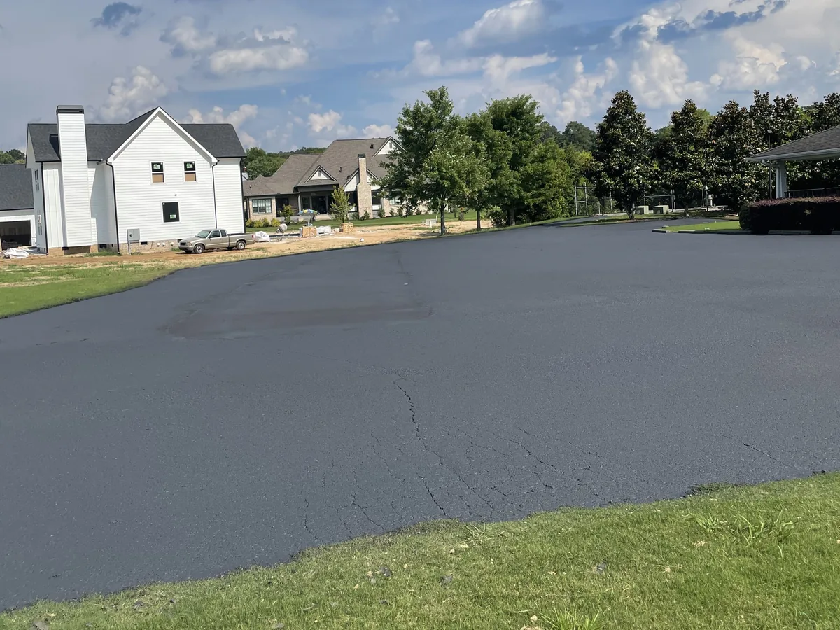 Dark sealed asphalt drive and parking area beside a home, the old surface cracks faintly showing through
